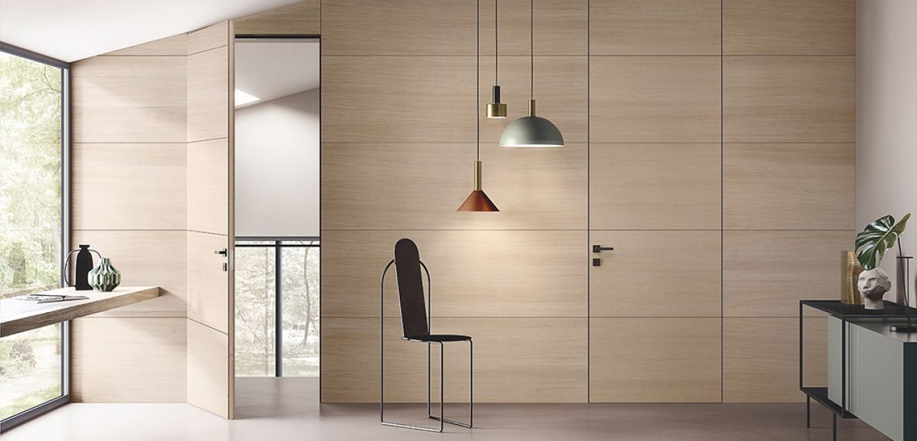 Porta laminata a filo muro integrata nel rivestimento in legno chiaro