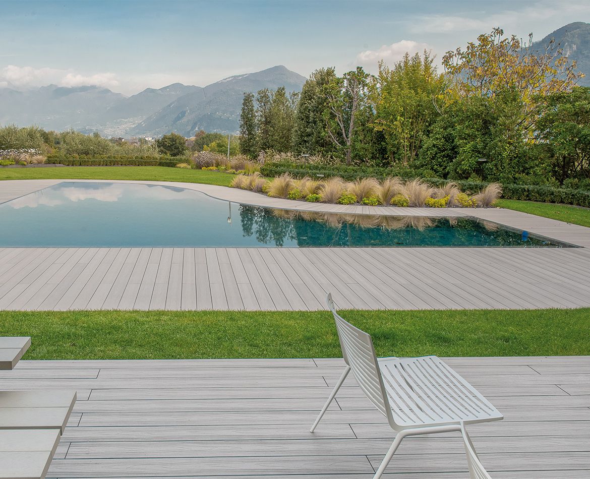 Area piscina con pavimentazione WPC effetto legno chiaro e panorama naturale sullo sfondo